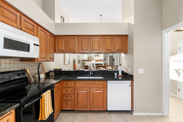 kitchen featuring white appliances, a sink, a towering ceiling, and brown cabinets