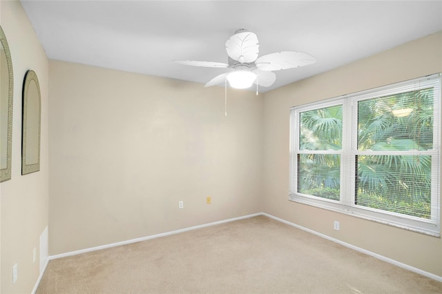 spare room featuring a ceiling fan, light carpet, and baseboards