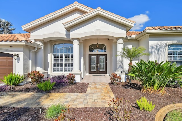 property entrance with an attached garage, stucco siding, a tiled roof, and french doors