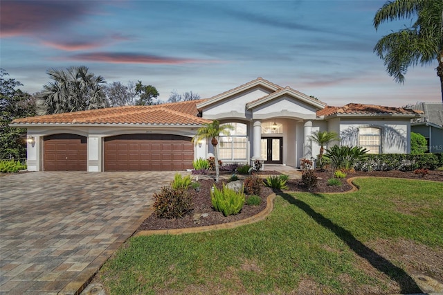 mediterranean / spanish home featuring an attached garage, french doors, decorative driveway, stucco siding, and a front yard