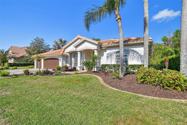 mediterranean / spanish home featuring a garage, stucco siding, a front lawn, and a tiled roof