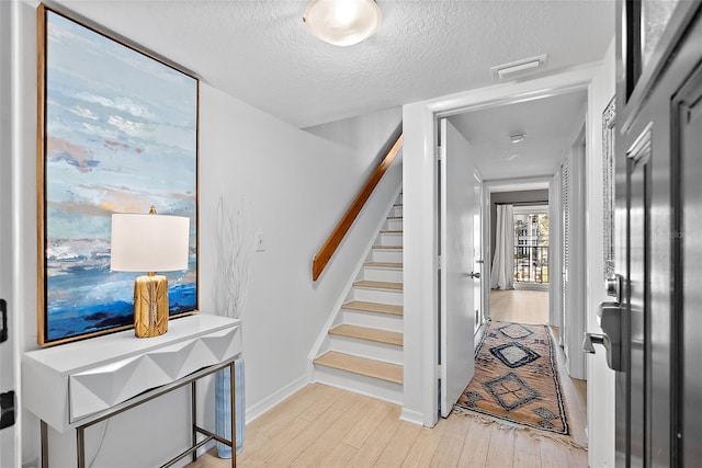 staircase with baseboards, a textured ceiling, visible vents, and wood finished floors