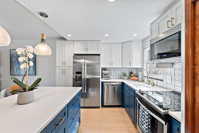 kitchen with blue cabinetry, stainless steel appliances, light countertops, white cabinets, and a sink