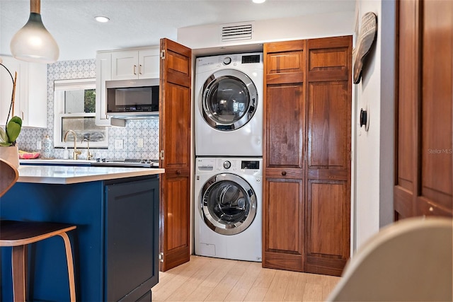 laundry area with stacked washer and clothes dryer, light wood finished floors, visible vents, a sink, and laundry area