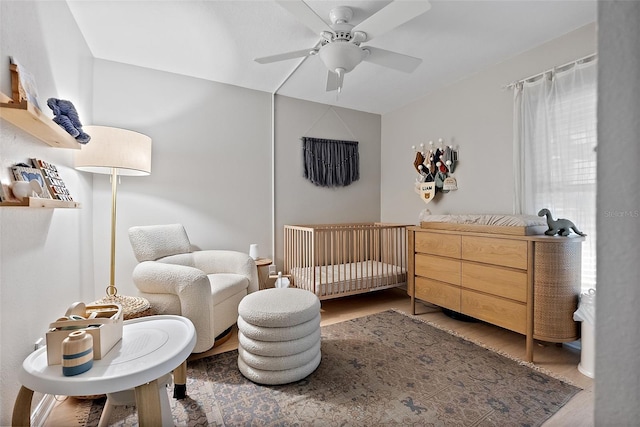 bedroom with a nursery area, ceiling fan, and wood finished floors