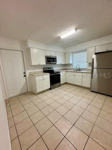 kitchen with a sink, light countertops, white cabinets, appliances with stainless steel finishes, and a textured ceiling