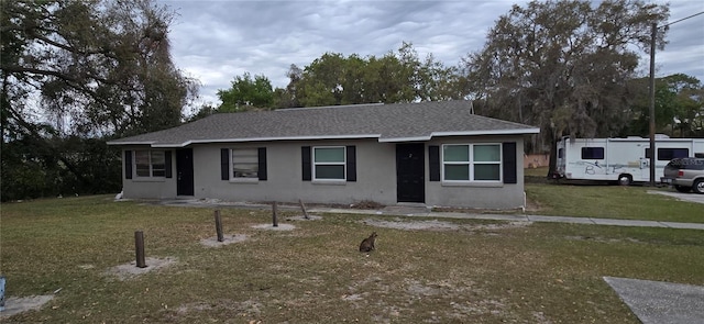 view of front of property with a shingled roof, a front yard, and stucco siding