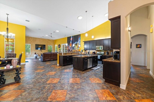 kitchen featuring arched walkways, appliances with stainless steel finishes, open floor plan, and a center island with sink