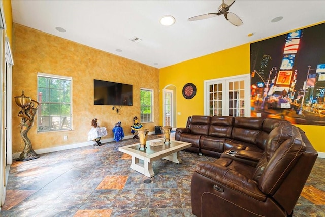 living area with arched walkways, ceiling fan, a wealth of natural light, and baseboards