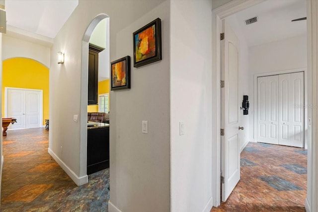 corridor featuring arched walkways, stone finish floor, visible vents, and baseboards