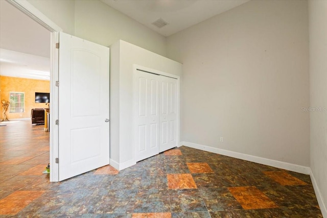 unfurnished bedroom featuring stone finish flooring, visible vents, baseboards, and a closet