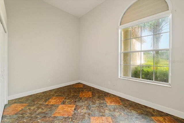 empty room featuring lofted ceiling, stone finish flooring, and baseboards