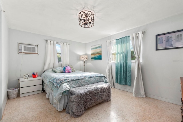 bedroom featuring speckled floor, a wall mounted AC, and baseboards