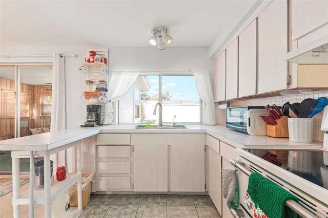 kitchen with under cabinet range hood, white electric range, a sink, light countertops, and tasteful backsplash