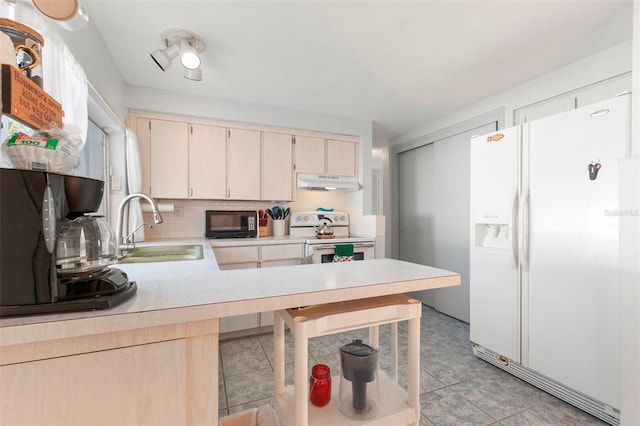 kitchen with white appliances, a peninsula, light countertops, under cabinet range hood, and a sink