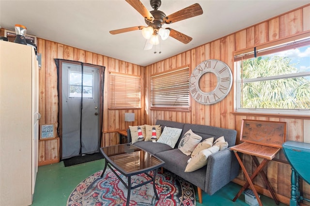 living area featuring wood walls, plenty of natural light, and a ceiling fan