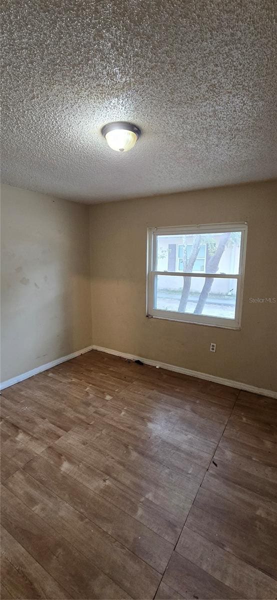 unfurnished room with baseboards, a textured ceiling, and wood finished floors