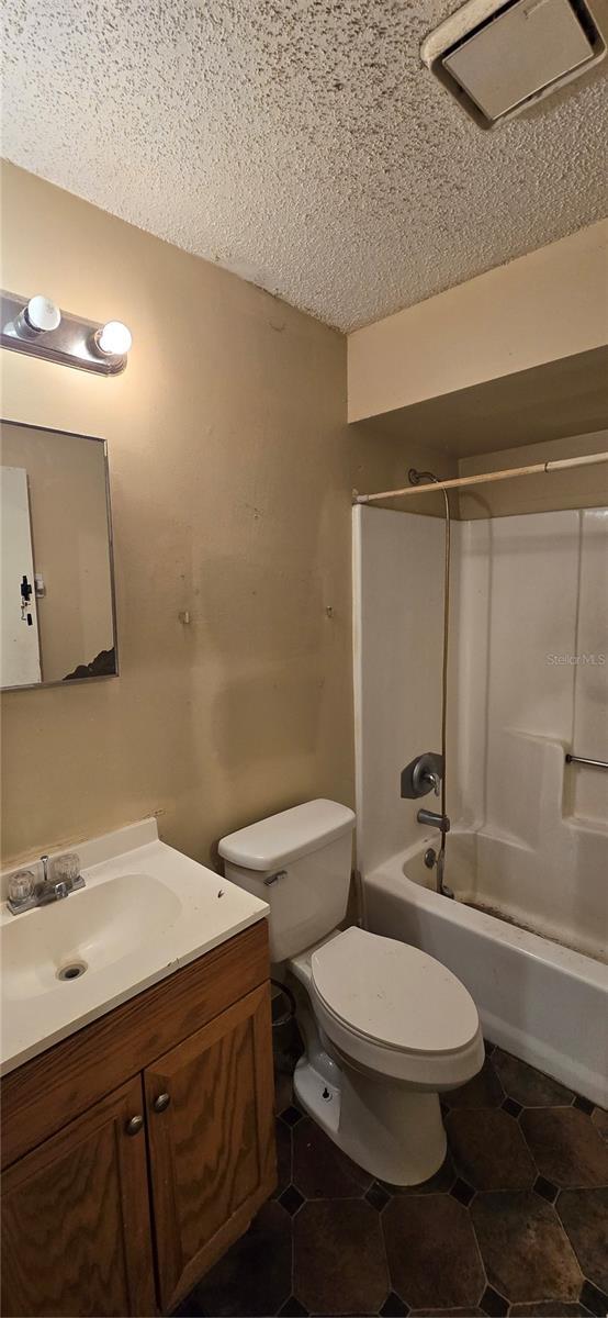 bathroom with tile patterned floors, toilet, a textured ceiling, shower / washtub combination, and vanity