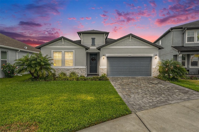 view of front facade featuring a garage, stone siding, a yard, decorative driveway, and stucco siding