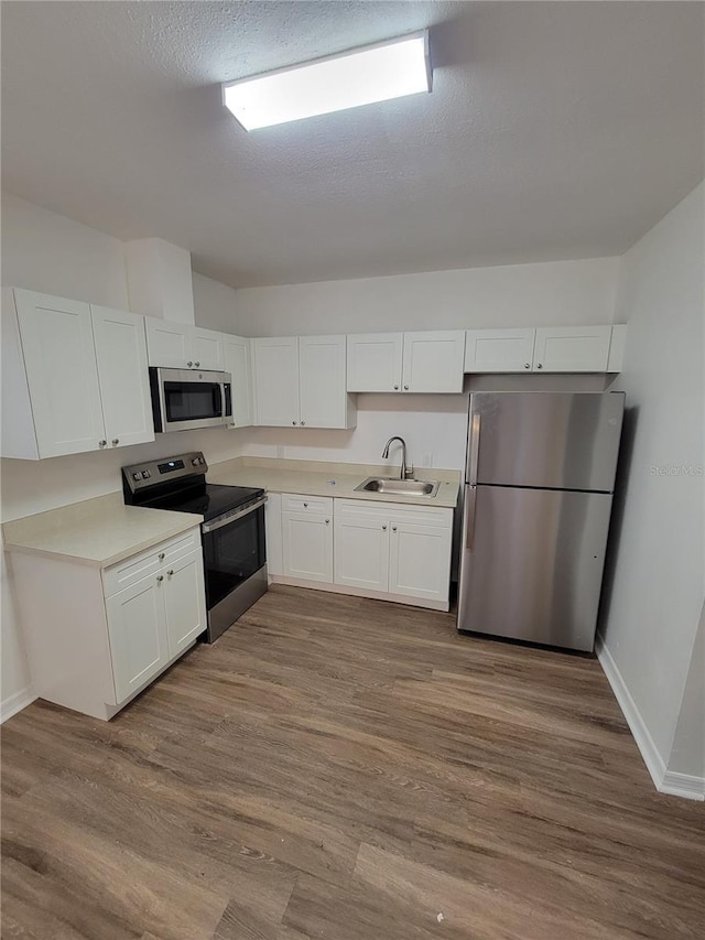 kitchen with stainless steel appliances, white cabinetry, a sink, and wood finished floors