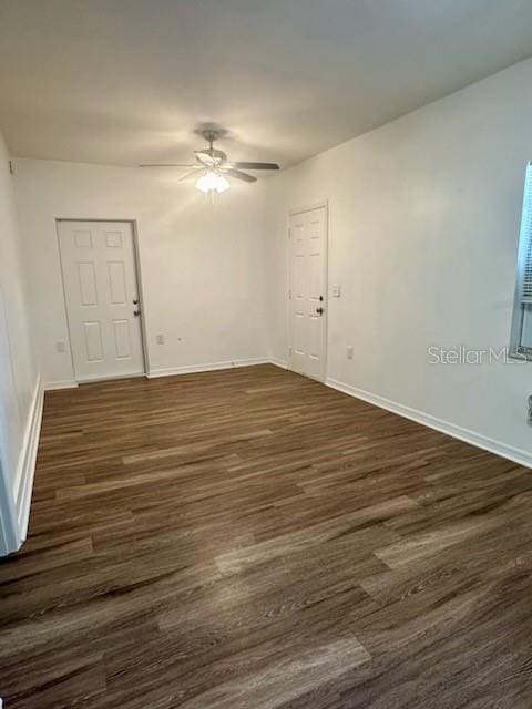 empty room with dark wood-type flooring, a ceiling fan, and baseboards