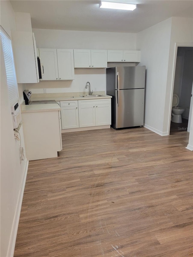 kitchen featuring stainless steel appliances, a sink, white cabinets, light wood-style floors, and light countertops