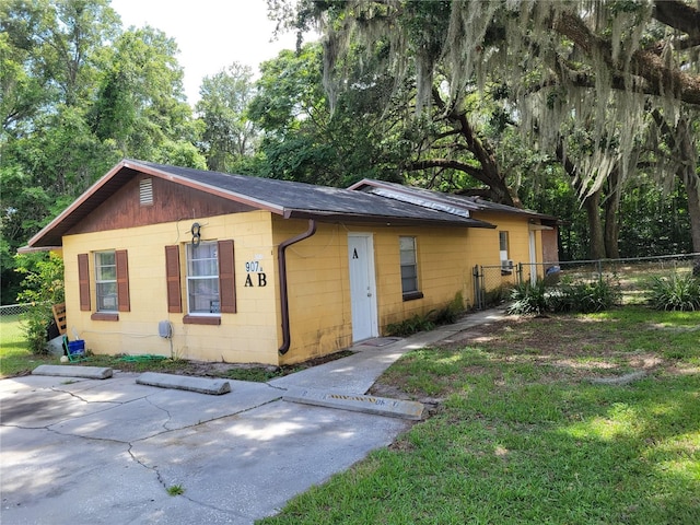 view of front of house featuring a shingled roof, fence, concrete block siding, and a front yard