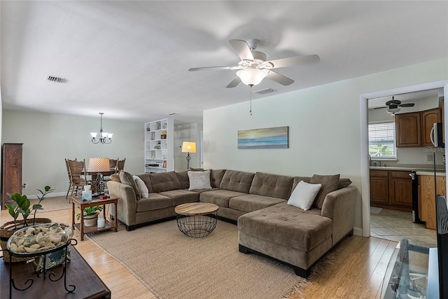 living area featuring ceiling fan with notable chandelier, visible vents, and light wood-style floors