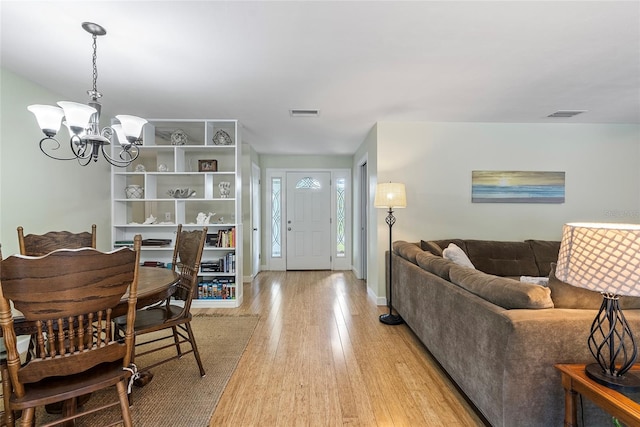 interior space featuring baseboards, visible vents, light wood finished floors, and an inviting chandelier