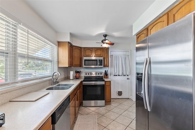 kitchen featuring brown cabinets, light countertops, appliances with stainless steel finishes, light tile patterned flooring, and a sink