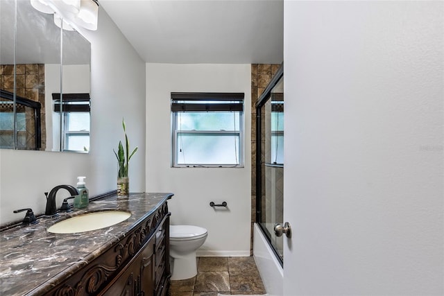 bathroom with toilet, shower / bath combination with glass door, vanity, baseboards, and stone finish floor