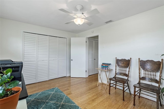 living area with baseboards, wood finished floors, visible vents, and a ceiling fan