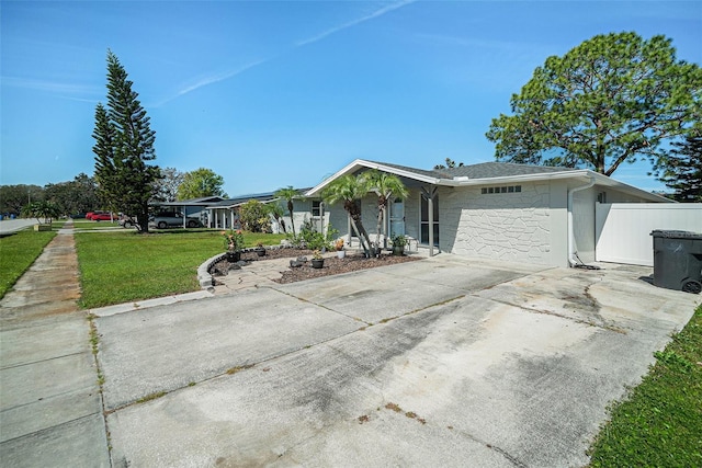 view of front of property featuring stone siding, a front yard, concrete driveway, and fence