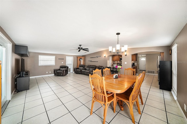 dining room with arched walkways, light tile patterned flooring, ceiling fan with notable chandelier, visible vents, and baseboards