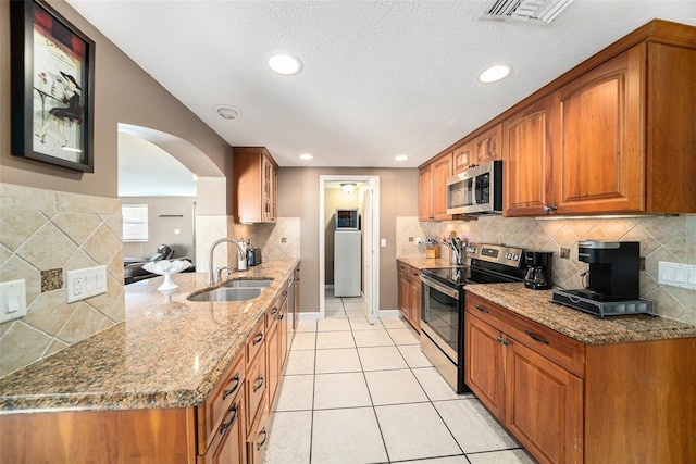 kitchen featuring visible vents, appliances with stainless steel finishes, brown cabinets, stone counters, and a sink