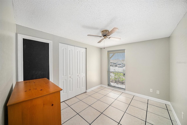 unfurnished bedroom featuring light tile patterned floors, a closet, a ceiling fan, a textured ceiling, and baseboards