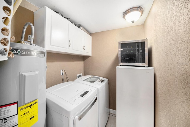 clothes washing area featuring water heater, a textured wall, washing machine and dryer, and cabinet space