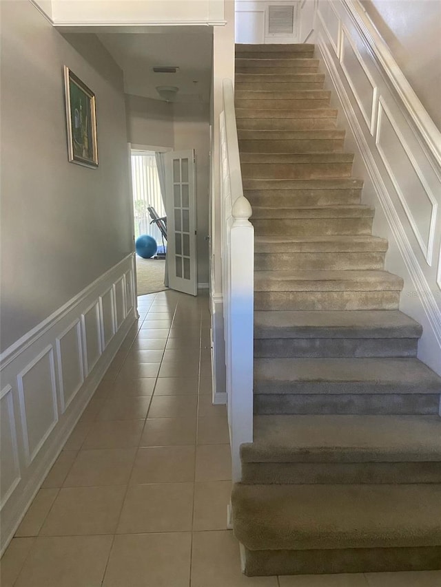 stairs with wainscoting, visible vents, a decorative wall, and tile patterned floors