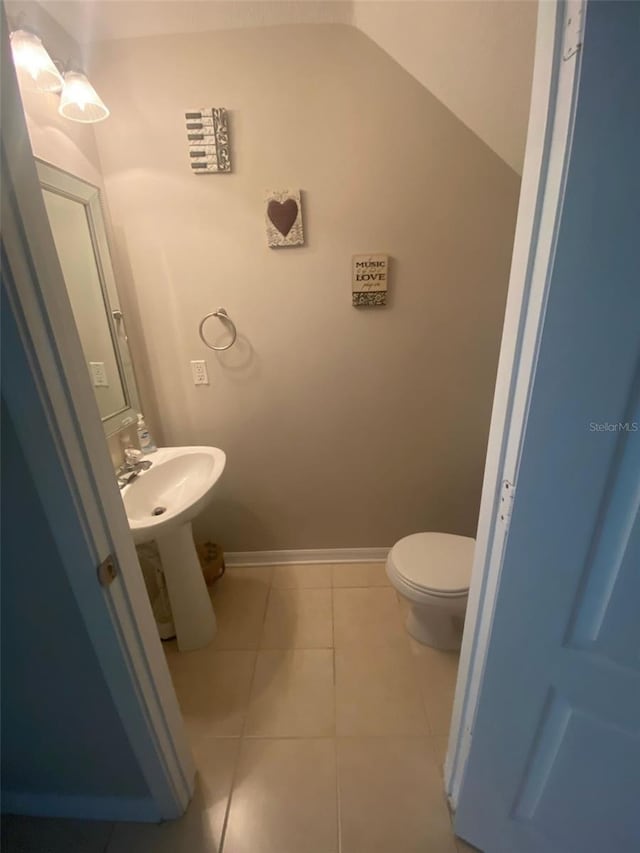 half bath with lofted ceiling, tile patterned flooring, baseboards, and toilet