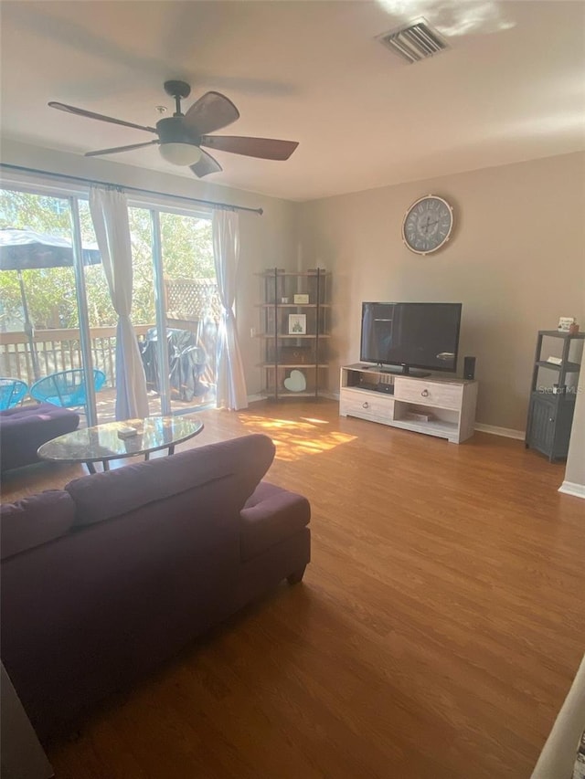 living area with a ceiling fan, wood finished floors, visible vents, and baseboards