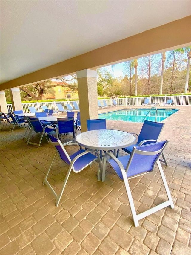 view of patio with outdoor dining space, fence, and a community pool