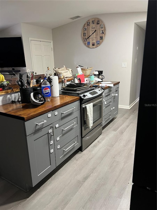 kitchen featuring stainless steel gas stove, light wood-style flooring, wood counters, and gray cabinets