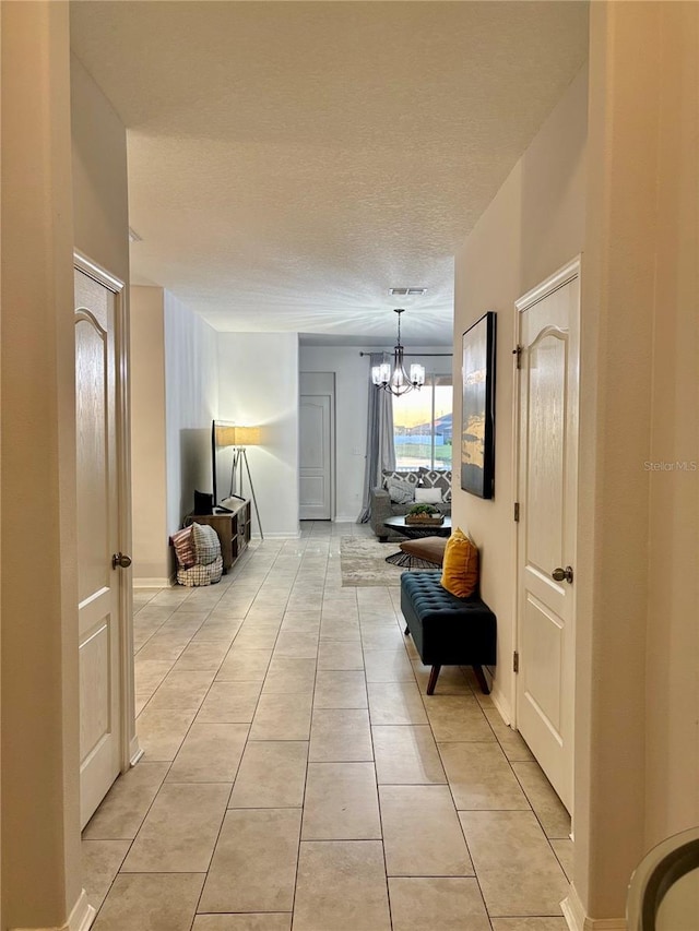 hall with visible vents, a chandelier, a textured ceiling, and light tile patterned flooring