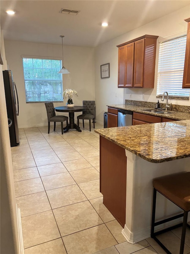 kitchen with light tile patterned floors, stainless steel appliances, a sink, brown cabinets, and dark stone countertops