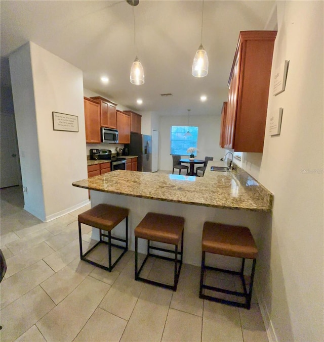 kitchen featuring appliances with stainless steel finishes, a breakfast bar, brown cabinetry, and a peninsula