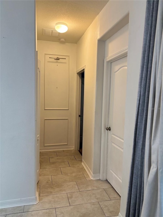 hall with baseboards, a textured ceiling, and light tile patterned flooring