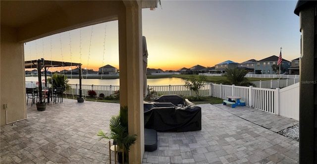 patio terrace at dusk featuring a water view and a fenced backyard