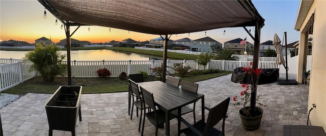 patio terrace at dusk featuring outdoor dining space, a water view, and a fenced backyard