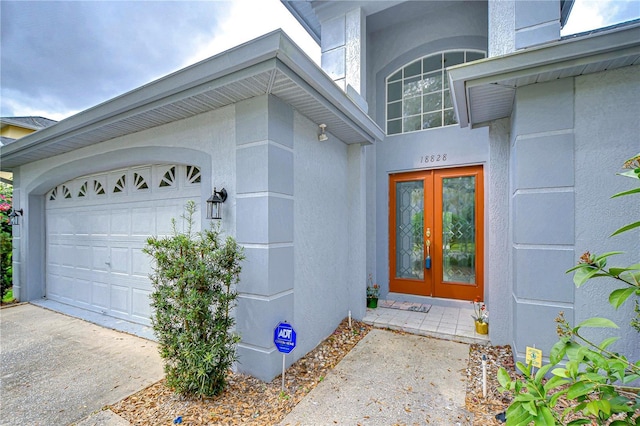 view of exterior entry with a garage, concrete driveway, french doors, and stucco siding