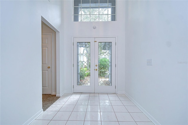 entryway with a towering ceiling, light tile patterned floors, baseboards, and french doors